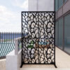 One black metal decorative screen with bird-and-branch cutouts standing on a tiled patio.