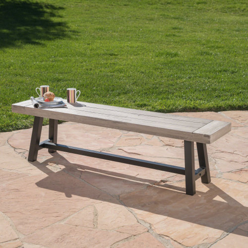 Light gray slatted acacia bench with a black metal frame on a stone patio.